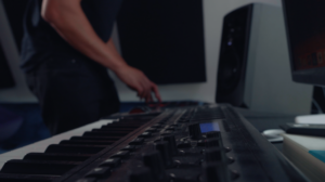 Screen_Shot_2021-09-17_at_8.34.53_PM-1925328 Close-up of hands working on a music production keyboard in a studio setting.