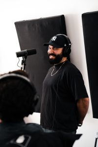 DSC05795 A bearded man wearing a cap and headphones, speaking into a microphone.