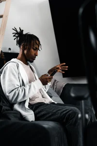 THS_RADDAR_PHOTOS_16 A young man in a white hoodie sitting in the studio, scrolling on his phone.